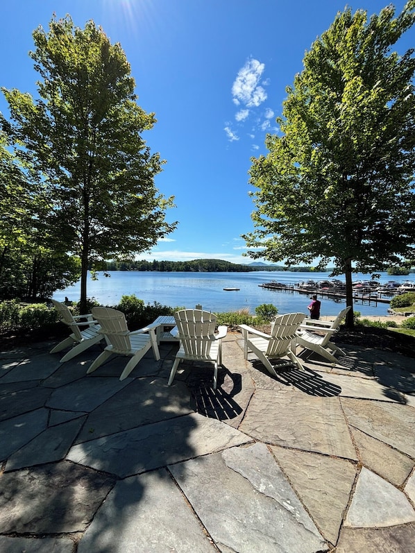 Une terrasse avec des fauteuils Adirondack donnant sur un lac où sont amarrés des bateaux.
