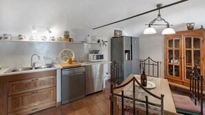A kitchen with a dishwasher, microwave, and refrigerator. There is a dining table with chairs and a cabinet with glass doors. - Montegrazie Holiday Home with Sea View, Private Terrace and Wi-Fi (Montegrazie)