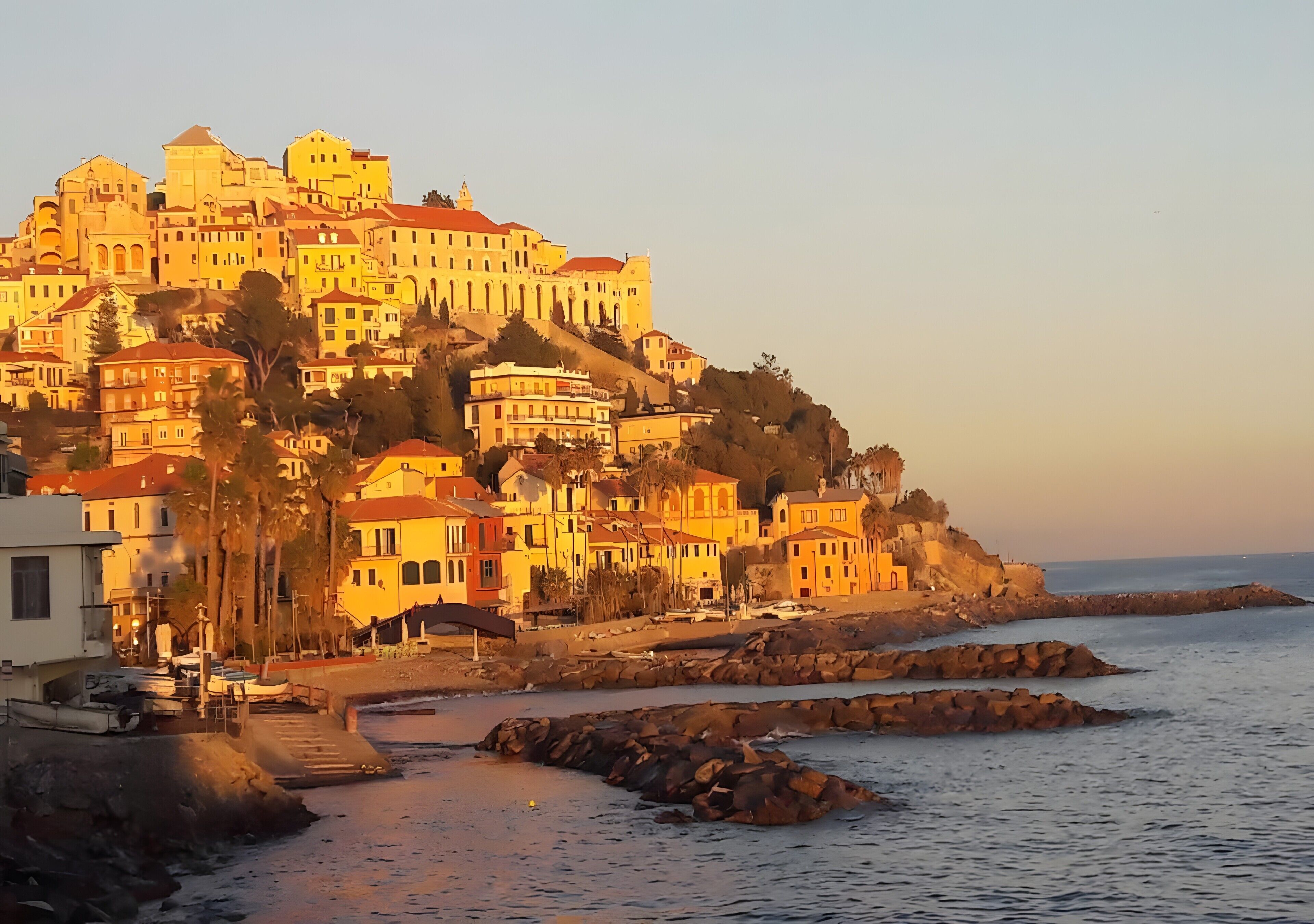 A coastal town with buildings on a hillside, a beach, and rocky outcrops.
