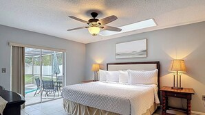 Une chambre d’hôtel comprenant un lit, deux lampes de chevet, un ventilateur de plafond, une fenêtre avec vue et une porte-fenêtre coulissante donnant sur un espace extérieur.