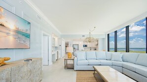 A modern living room with a large sectional sofa, a wooden coffee table, and a view of the ocean through large windows.