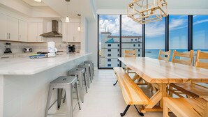 A modern kitchen with a large island, bar stools, and a view of the ocean.
