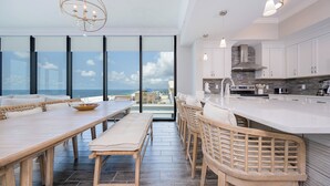 A modern kitchen with a large island, white cabinets, and a view of the ocean.