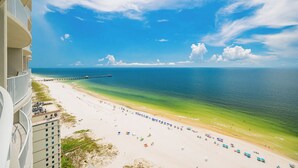 A beach with a pier extending into the ocean, a white sandy shore, and a clear blue sky.