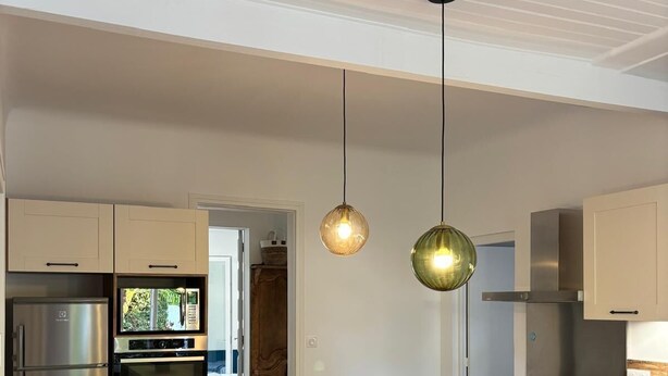 A modern kitchen with a central island, stainless steel appliances, and hanging pendant lights.