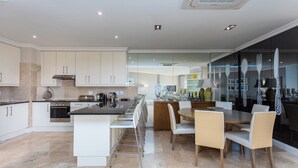 A modern kitchen with white cabinets, a central island with bar stools, and a dining area with wicker chairs.
