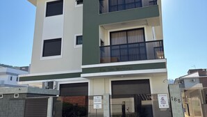 A modern multi-story residential building with a flat roof, large windows, and a balcony.