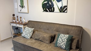 A living room with a grey sofa, patterned cushions, a small side table with decorative items, and a colorful rug.