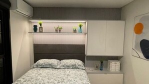A bedroom with a bed, bedside tables, a wardrobe, and a wall-mounted shelf with plants.
