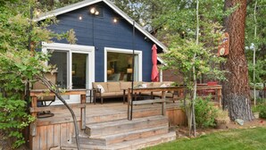 A blue cabin with a wooden deck, outdoor seating, and a large tree nearby. - Yaya’s: 4BR Retreat | Lake • Golf • Ski (Tahoe Vista)