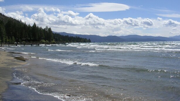 A beach with waves, a pier, and a forested hill in the background. - Yaya’s: 4BR Retreat | Lake • Golf • Ski (Tahoe Vista)