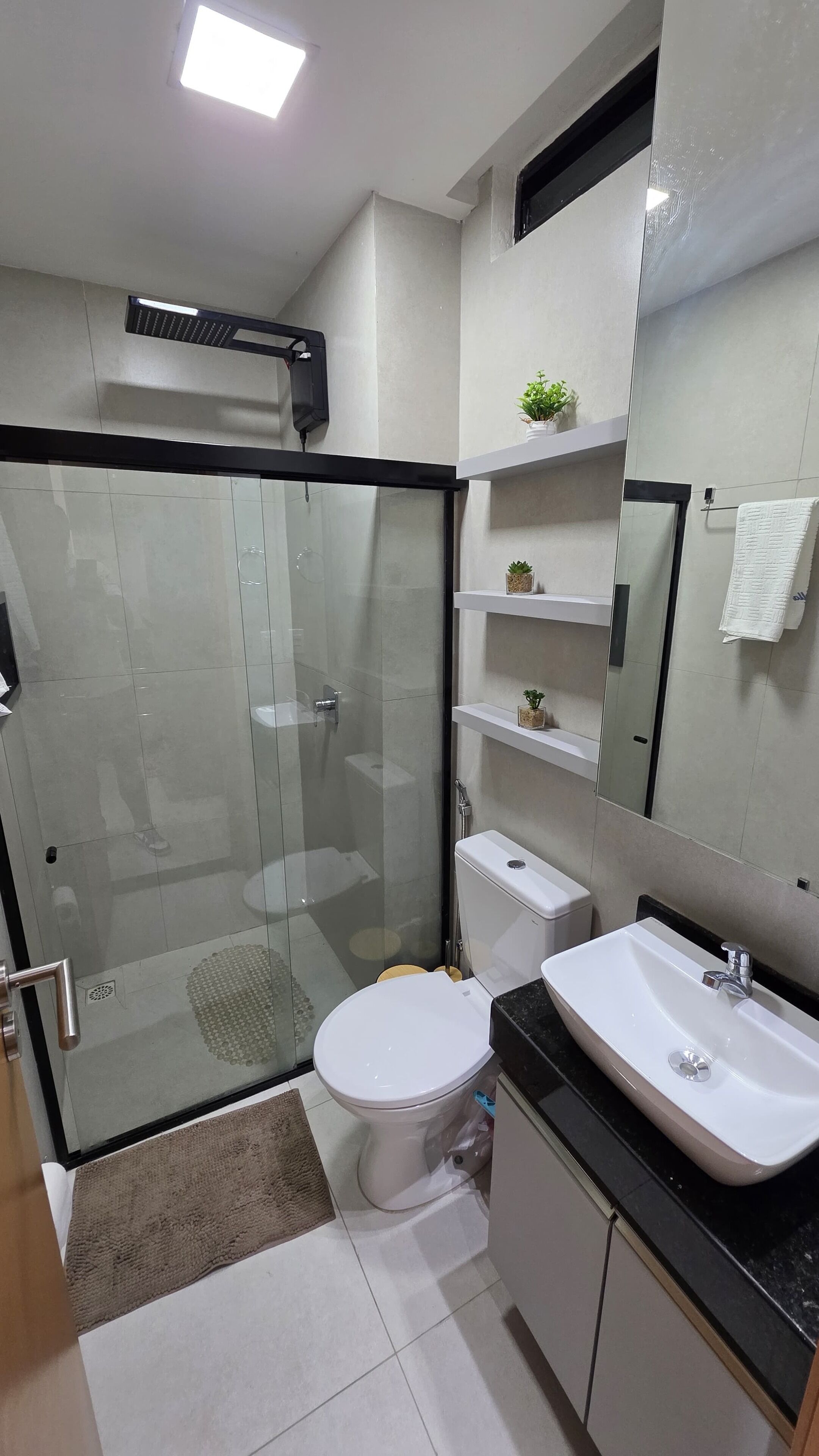 Un baño moderno con ducha de vidrio, inodoro blanco, lavamanos con encimera negra y espejo sobre el lavamanos.
