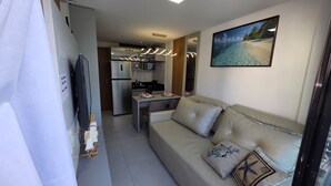 Ein modernes Wohnzimmer mit einer Couch, einem Flachbildfernseher und einem durch eine offene Tür einsehbarer Küchenbereich.