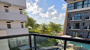 Ein Balkon mit einem Glastisch und Stühlen, mit Blick auf einen Swimmingpool und ein Gebäude mit mehreren Balkonen.