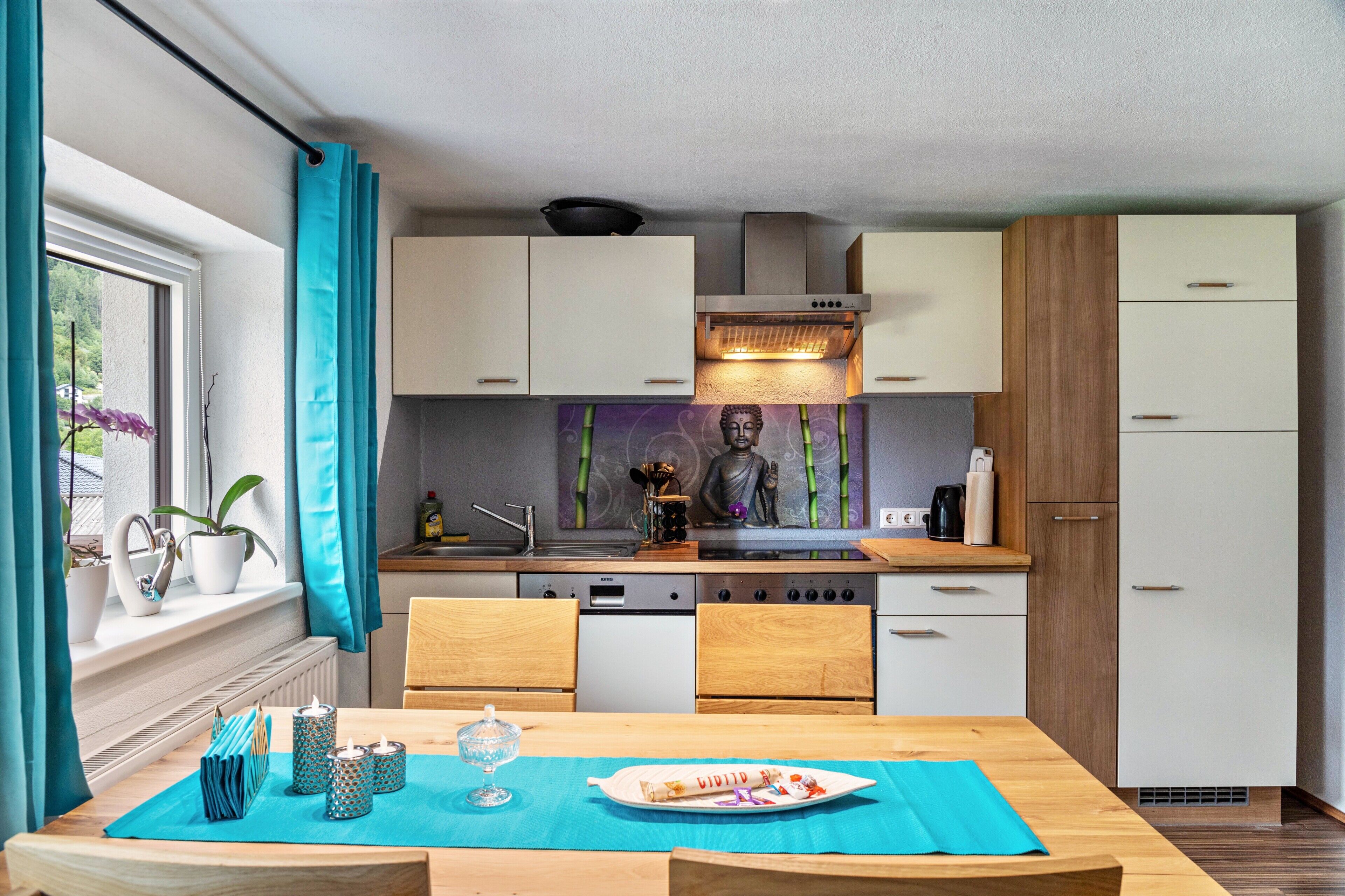 Una cocina compacta con zona de comedor, una estatua de Buda y un ventanal con cortinas.