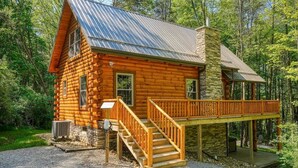 Une cabane en rondins avec une cheminée en pierre, une terrasse en bois et un escalier menant à l’entrée.