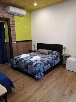 A bedroom with a bed, a nightstand, an air conditioning unit, and a small white appliance. - Marina Club (Giardini Naxos)