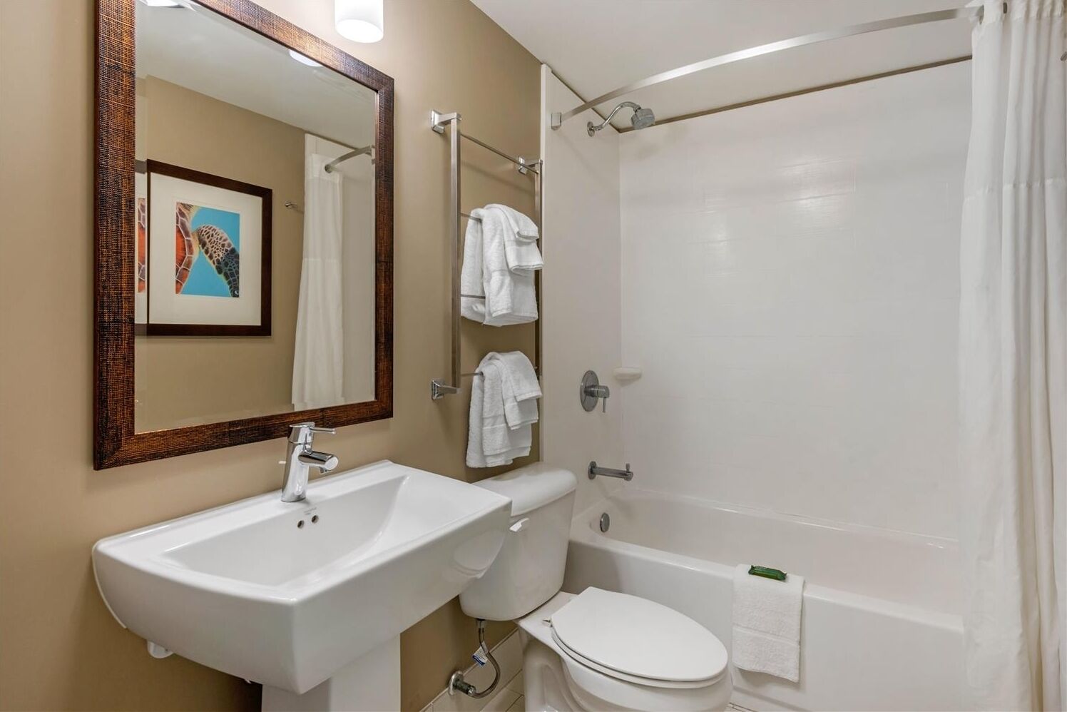 A bathroom with a white sink, toilet, and bathtub. There is a framed picture on the wall above the sink.