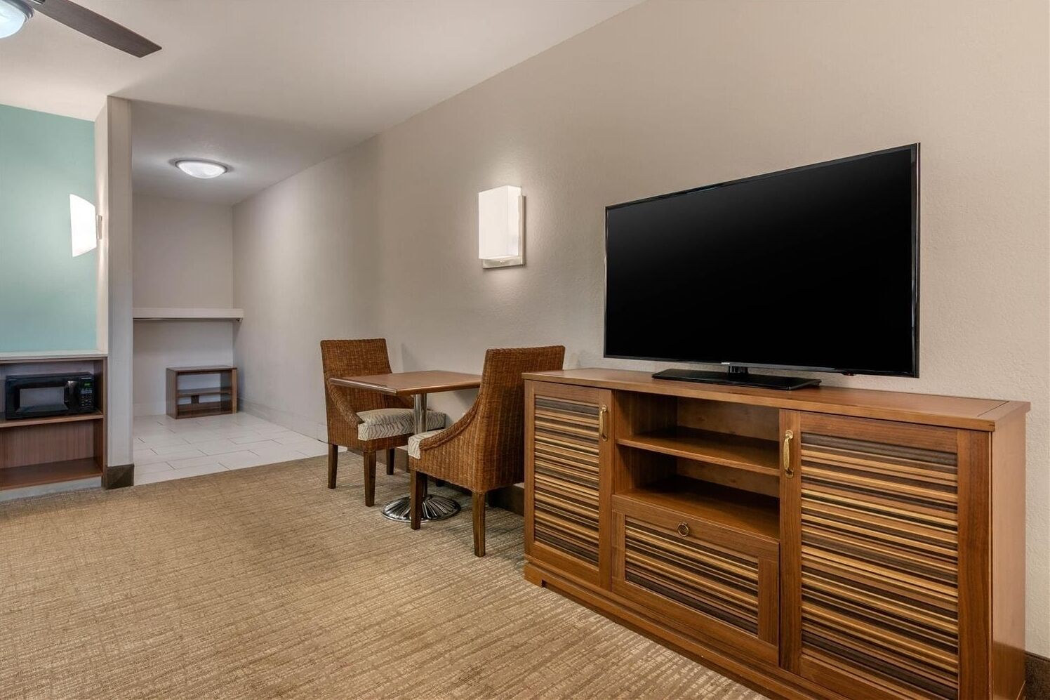 Une chambre d’hôtel équipée d’un téléviseur à écran plat, d’une table à manger avec des chaises, d’un four à micro-ondes et d’un petit meuble de rangement.