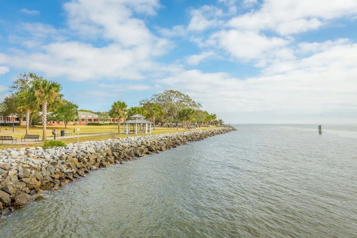 A coastal walkway with a stone wall, benches, and a gazebo.