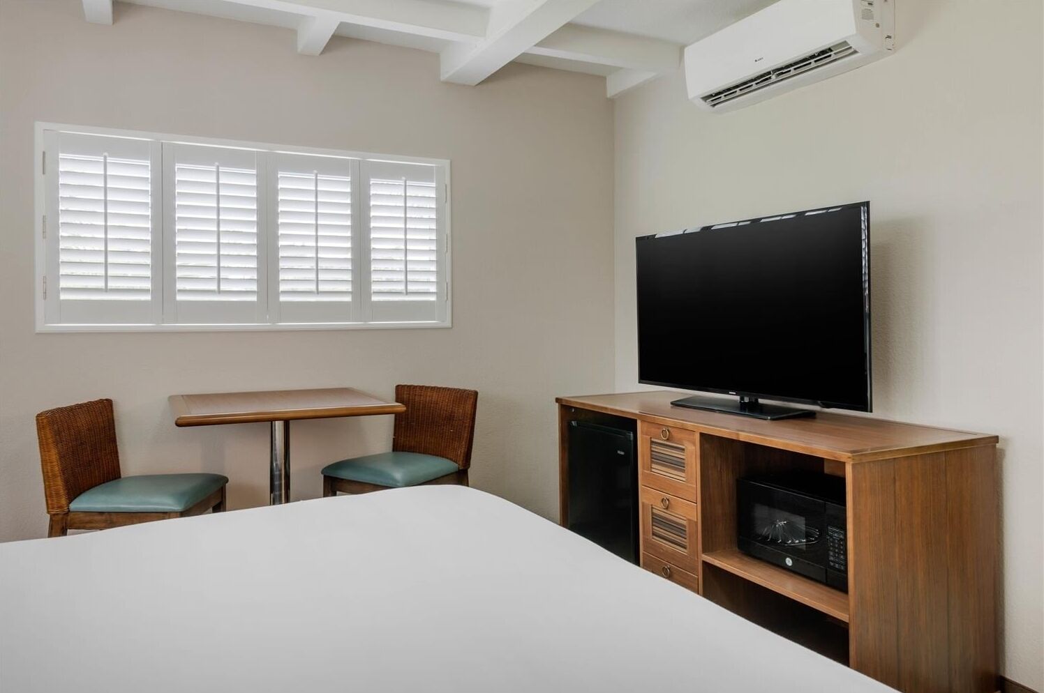 A hotel room with a bed, a TV, a desk, two chairs, and a window with blinds.