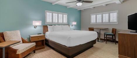 Una habitación de hotel con cama, escritorio, silla, televisión y ventilador de techo.