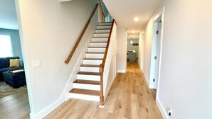 Een modern interieur met een houten trap naar een tweede verdieping, een gang met houten vloeren, en een zichtbare keuken op de achtergrond.