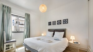 A bedroom with a bed, bedside lamps, a small table, and a window with curtains. - Luzia Apartment in Tavira (Tavira)