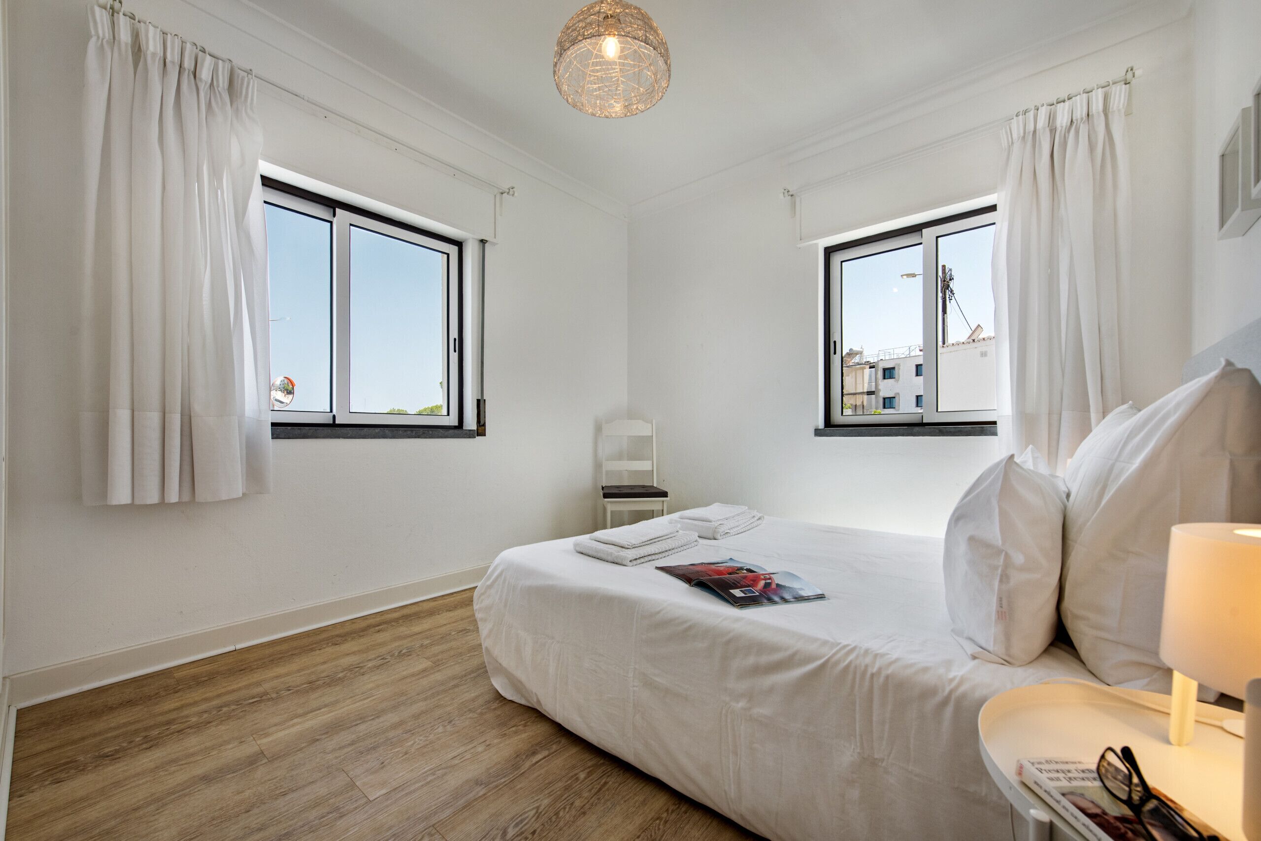 Quarto com cama grande, duas janelas, uma cadeira e uma luminária.