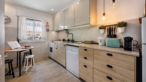 A modern kitchen with wooden cabinets, a dishwasher, a sink, and a window with curtains. - Luzia Apartment in Tavira (Tavira)