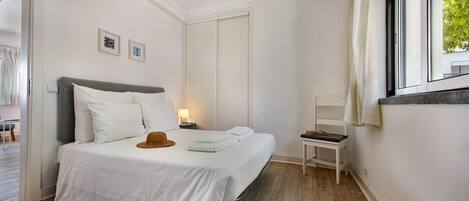 A bedroom with a bed, bedside table, lamp, and a window with curtains.