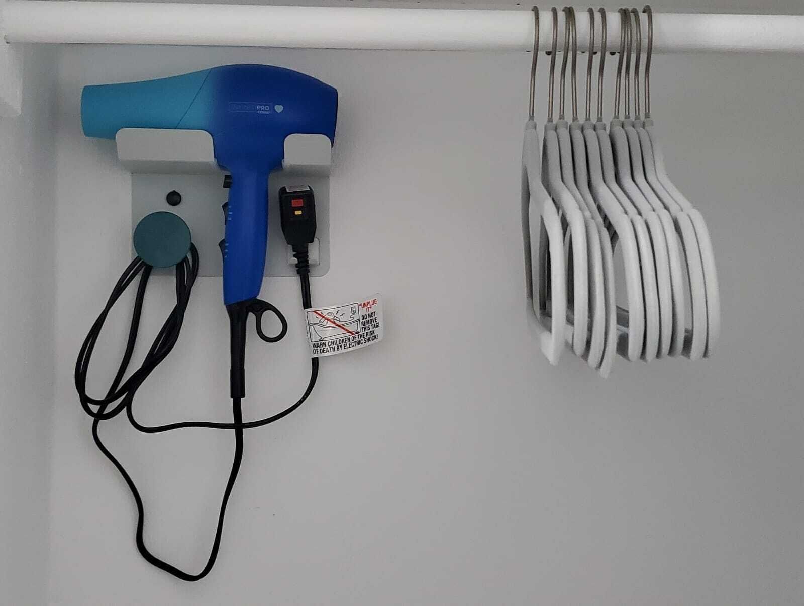 Ein blauer Fön und ein weißes Kabel, das an einer Wand aufgewickelt ist.