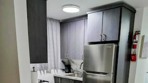 Une cuisine compacte dotée d’un plan de travail en marbre, d’appareils électroménagers en acier inoxydable et d’armoires en bois foncé.