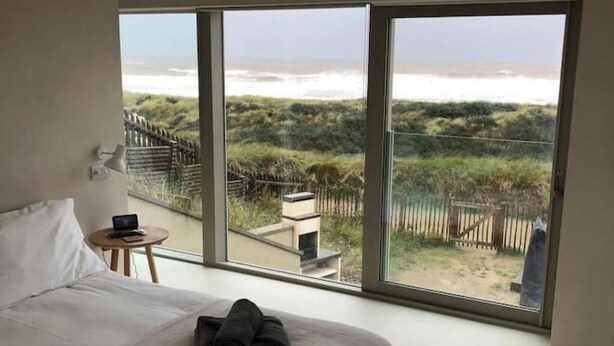 Un dormitorio con un ventanal grande que da a una playa y dunas.
