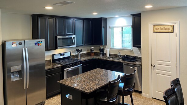 A modern kitchen with dark cabinets, stainless steel appliances, granite countertops, and a built-in island with bar stools. - 4-bedroom house in welcoming Missouri City with WiFi, AC near NRG Stadium (Missouri City)