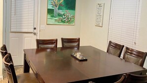 A dining room with a large rectangular table, six wooden chairs, a ceiling light, a door with blinds, a framed picture, and a wall-mounted sign. - 4-bedroom house in welcoming Missouri City with WiFi, AC near NRG Stadium (Missouri City)