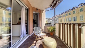 A balcony with a wicker chair, a round ottoman, and a potted plant.