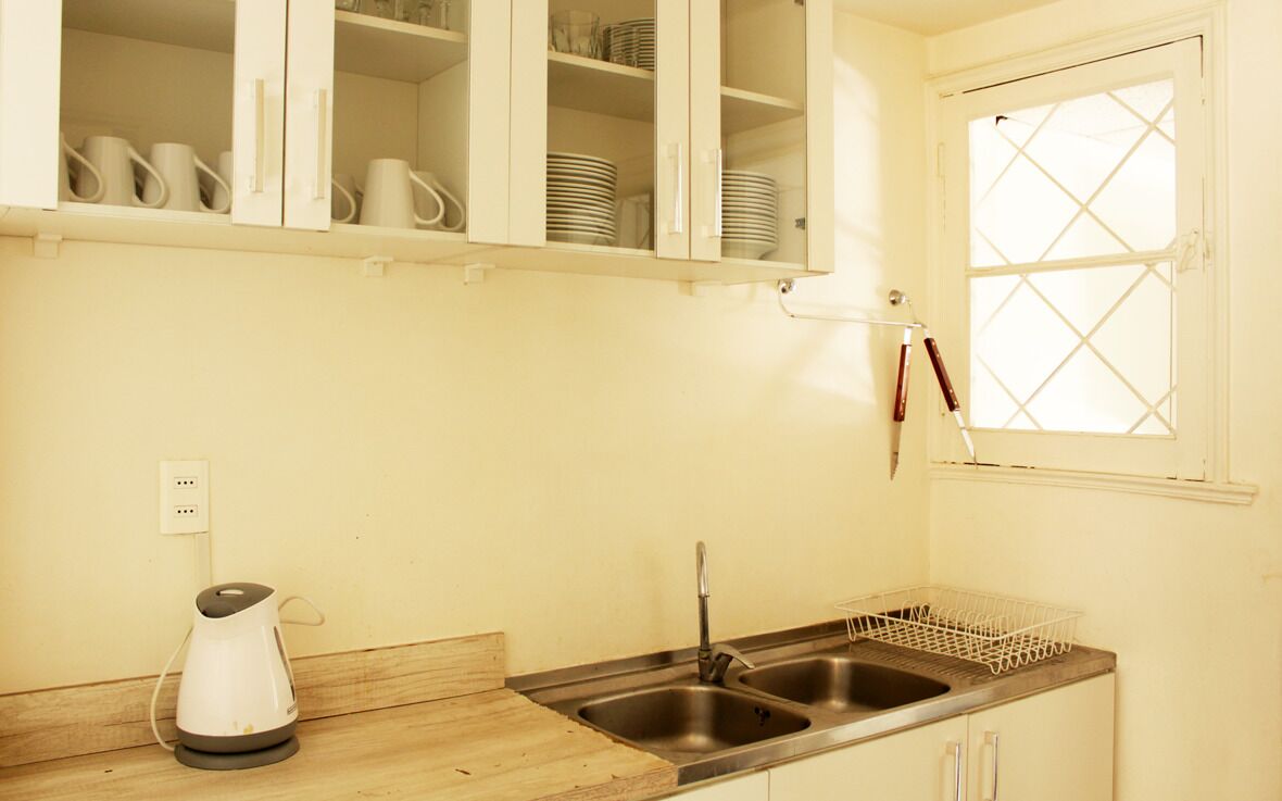 A kitchen with white cabinets, a double sink, a kettle, and a window with a diamond pattern.