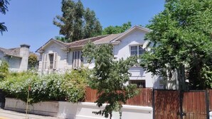 A two-story house with a white facade, a brown roof, and a wooden fence. - Casa y patio en mejor barrio de Santiago (Santiago)