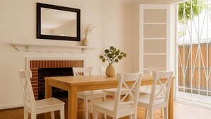 A dining area with a wooden table and white chairs, a fireplace, a mirror, and a window with a view of greenery. - Casa y patio en mejor barrio de Santiago (Santiago)