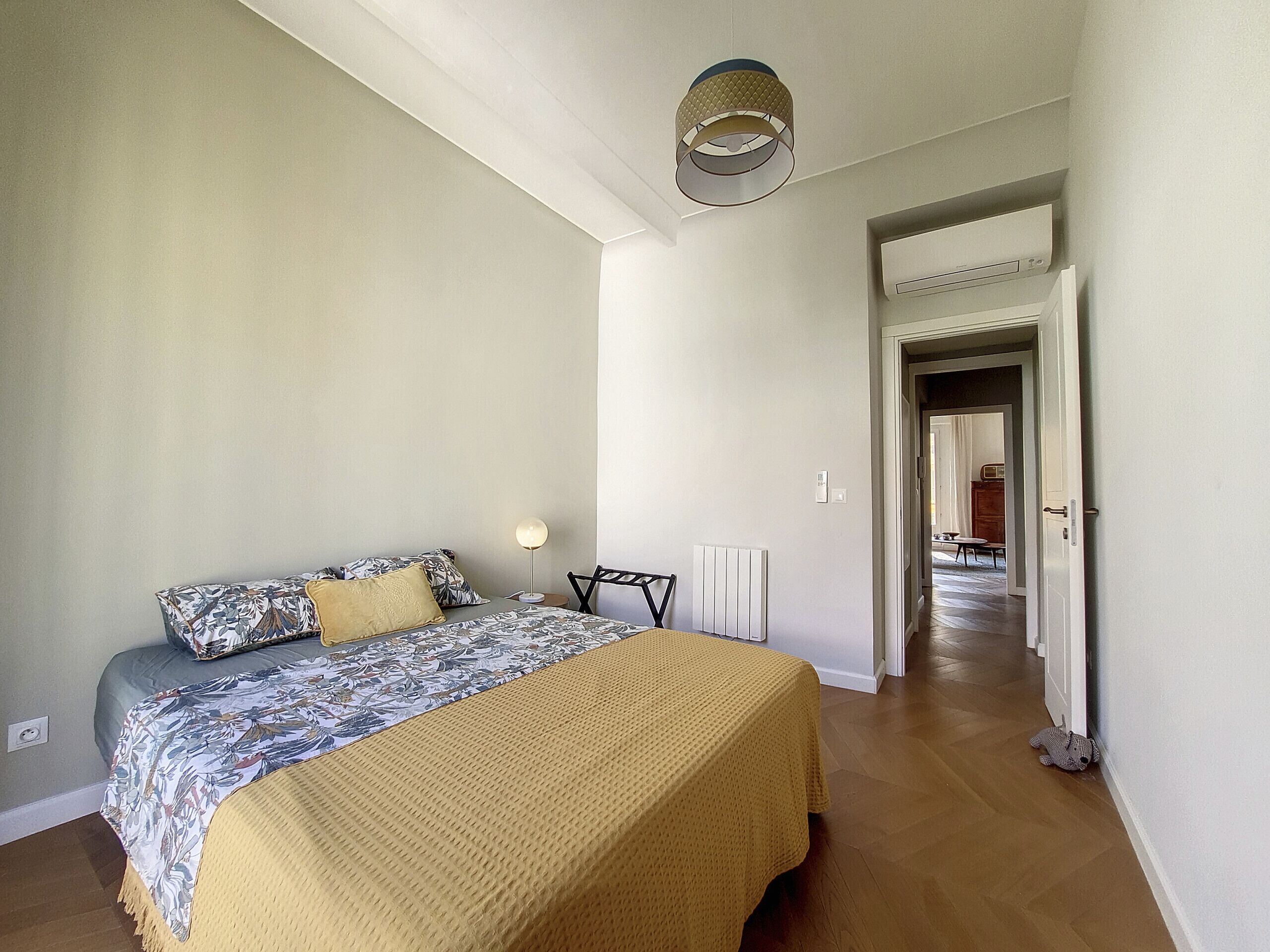 Une chambre à coucher avec un lit, une table de chevet, une lampe et une vue sur un couloir.