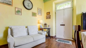 A room with a white sofa, a wooden floor, a clock, a sewing machine, and a door.
