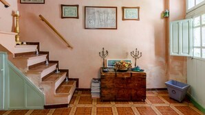 A staircase leading to a landing with a wooden chest of drawers, framed architectural drawings, and a candelabra on the wall.