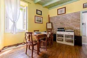 Un comedor con una mesa y sillas de madera, un armario blanco con libros y una ventana con cortinas.