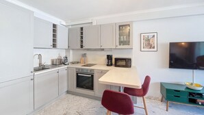 Une cuisine compacte avec des meubles blancs, un four à micro-ondes, une machine à café et un coin repas comprenant une table et deux chaises rouges.