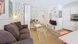 Kompakti oleskelutila, jossa on sohva, lasinen sohvapöytä, ruokapöytä ja pieni keittiö.