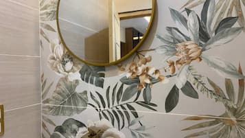Une salle de bain avec un papier peint à motifs floraux, un miroir rond et un robinet doré.