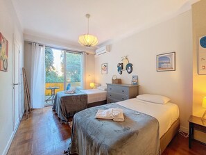 A hotel room with two beds, a balcony, a dining table, and a view of greenery. - N&J - MELODIE DU SUD - Central - Near Beach (Niza)