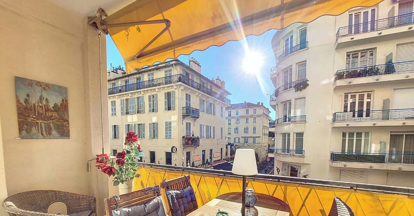 A balcony with a yellow awning, wicker furniture, a table with a vase of flowers, and a painting on the wall.