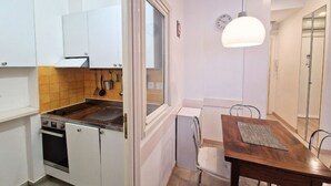 A compact kitchen with white cabinets, a built-in stove, and a dining area with a wooden table and chairs. - N&J - SAVOY PROMENADE - Central - Near Beach (Niza)